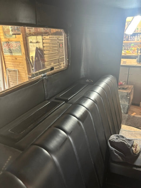 Pleated black vinyl bench seat with speaker grilles set into the panel behind it
